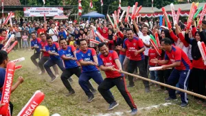 Peserta lomba tarik tambang membawa balon tepuk merah untuk memeriahkan perayaan kemerdekaan.